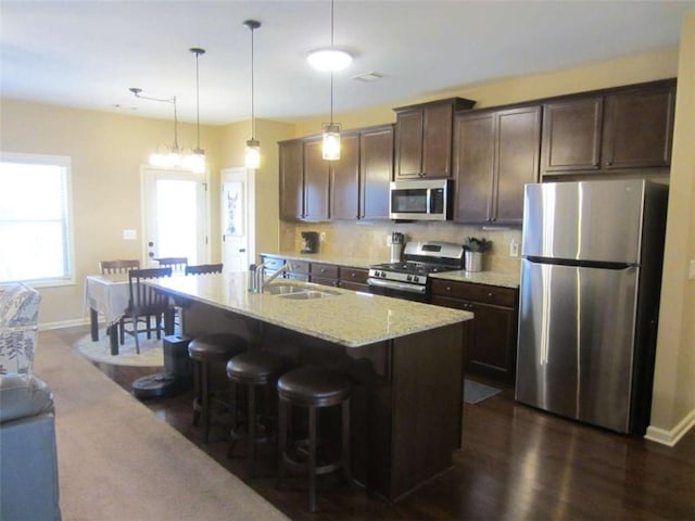 kitchen featuring a center island with sink, a sink, tasteful backsplash, dark brown cabinetry, and appliances with stainless steel finishes