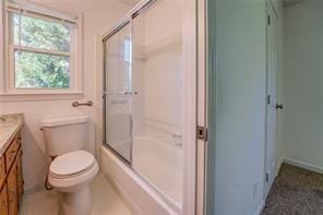 bathroom featuring toilet, bath / shower combo with glass door, and vanity