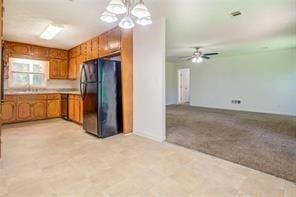 kitchen featuring pendant lighting, light countertops, brown cabinetry, freestanding refrigerator, and light carpet