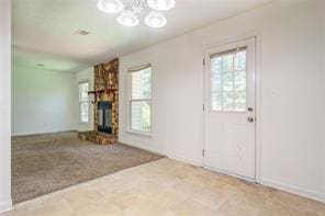 unfurnished living room featuring a chandelier, a stone fireplace, plenty of natural light, and carpet flooring