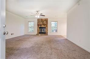 unfurnished living room with carpet floors, a stone fireplace, and a ceiling fan