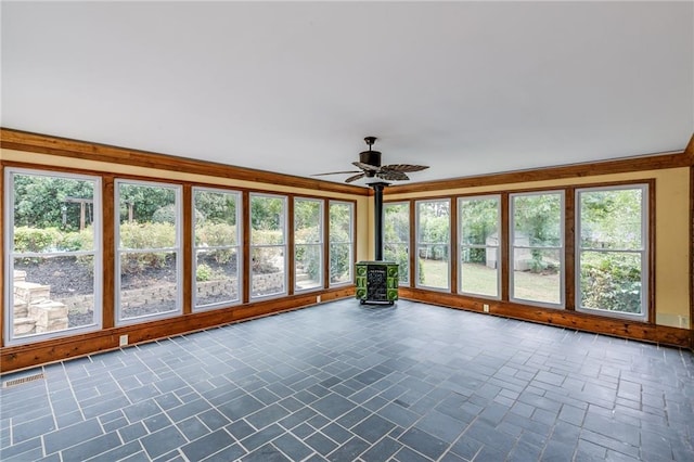 unfurnished sunroom with a ceiling fan, a wealth of natural light, a wood stove, and visible vents