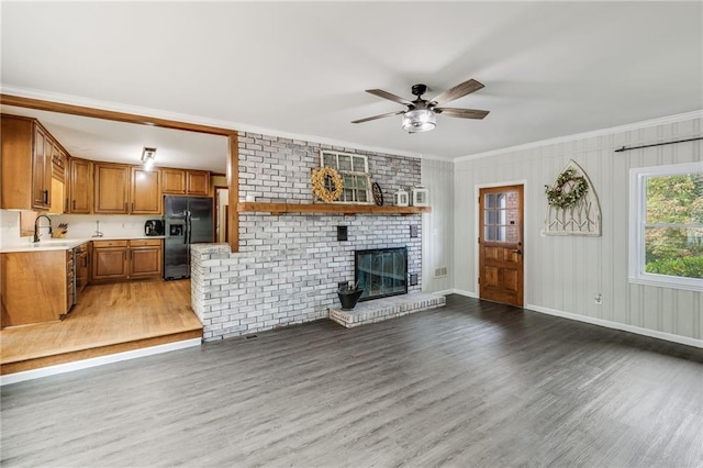 unfurnished living room with crown molding, a brick fireplace, a sink, and light wood-style flooring