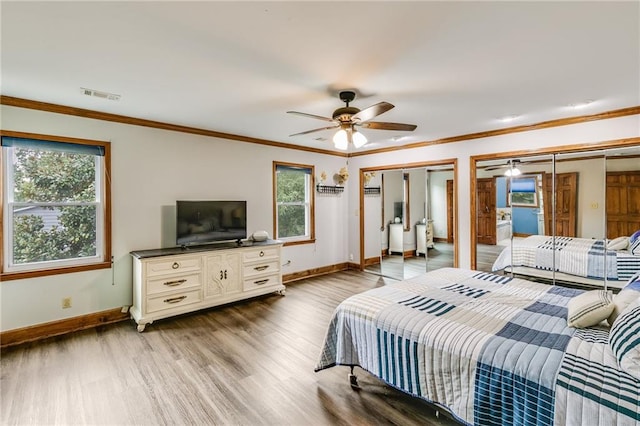 bedroom with ornamental molding, wood finished floors, visible vents, and multiple closets