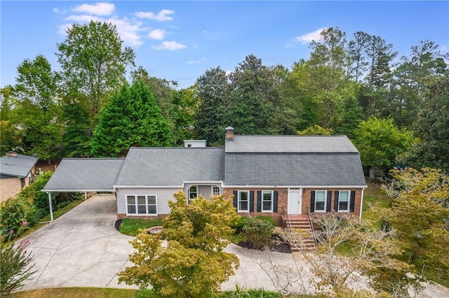 colonial inspired home featuring brick siding, a gambrel roof, concrete driveway, roof with shingles, and a carport