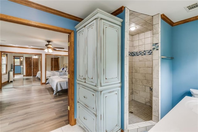 full bath featuring visible vents, ornamental molding, ceiling fan, wood finished floors, and tiled shower