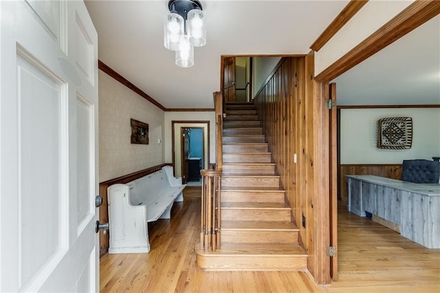 stairway featuring ornamental molding, a wainscoted wall, wallpapered walls, and wood finished floors