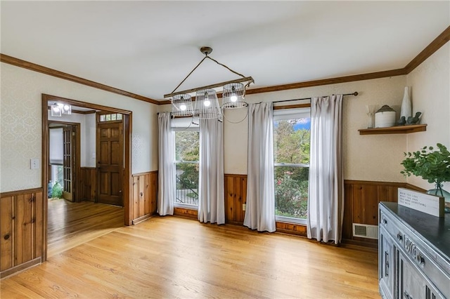 unfurnished dining area with a wainscoted wall, light wood-type flooring, and visible vents