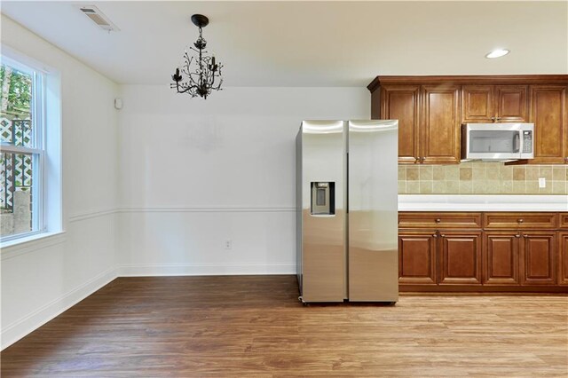 kitchen with hanging light fixtures, an inviting chandelier, tasteful backsplash, appliances with stainless steel finishes, and light wood-type flooring