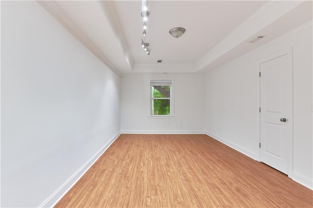 empty room with a raised ceiling, light wood-type flooring, ornamental molding, and track lighting