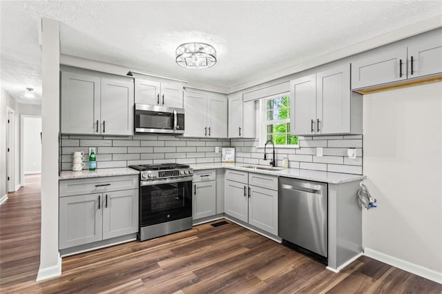 kitchen featuring stainless steel appliances, gray cabinetry, a sink, a textured ceiling, and baseboards