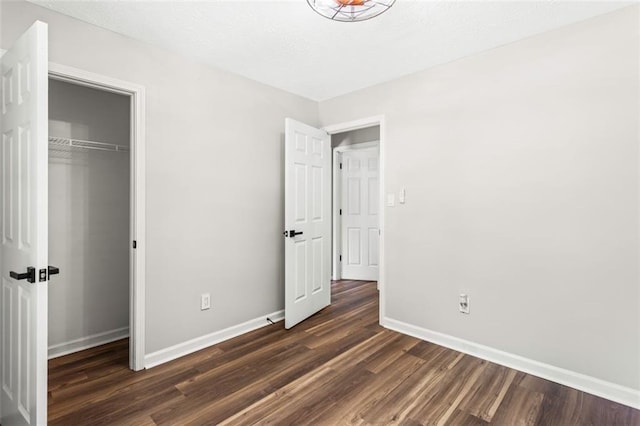 unfurnished bedroom featuring dark wood finished floors, baseboards, and a closet