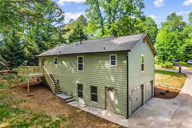 back of house with stairs, a deck, an attached garage, concrete driveway, and roof with shingles