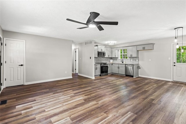 unfurnished living room with ceiling fan, plenty of natural light, dark wood finished floors, baseboards, and a textured ceiling