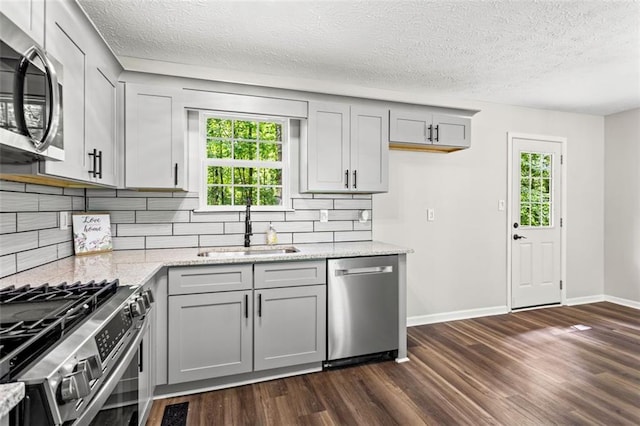 kitchen featuring stainless steel appliances, a sink, gray cabinets, dark wood-style flooring, and a textured ceiling
