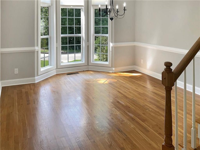 unfurnished dining area with wood-type flooring and an inviting chandelier