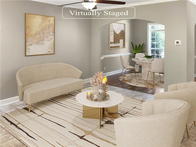 living room with ornamental molding, arched walkways, ceiling fan, and baseboards