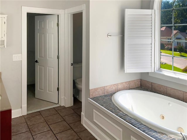 bathroom with tile patterned flooring, tiled tub, and toilet