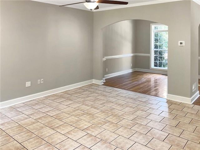 empty room with baseboards, crown molding, arched walkways, and a ceiling fan