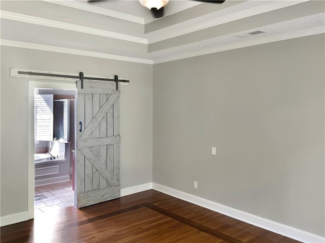 spare room featuring a barn door, hardwood / wood-style floors, ceiling fan, and ornamental molding