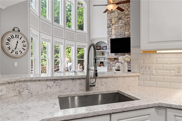 3560 Greenside Ct, Dacula, GA 30019 - kitchen featuring a ceiling fan, backsplash, white cabinets, light stone countertops, and a fireplace