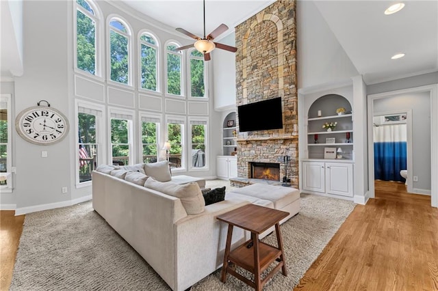 3560 Greenside Ct, Dacula, GA 30019 - living room featuring a fireplace, a towering ceiling, crown molding, a ceiling fan, and light wood finished floors