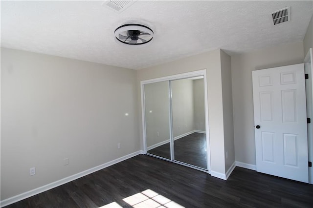 unfurnished bedroom with dark hardwood / wood-style floors, a textured ceiling, and a closet