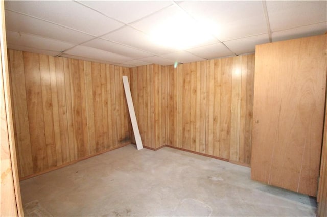 basement with a drop ceiling and wooden walls