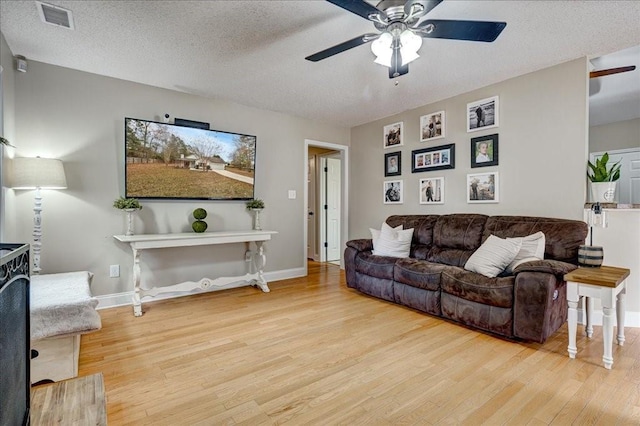 living room with ceiling fan, light hardwood / wood-style floors, and a textured ceiling