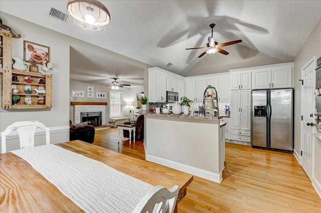 kitchen with white cabinetry, lofted ceiling, light wood-type flooring, stainless steel appliances, and a textured ceiling