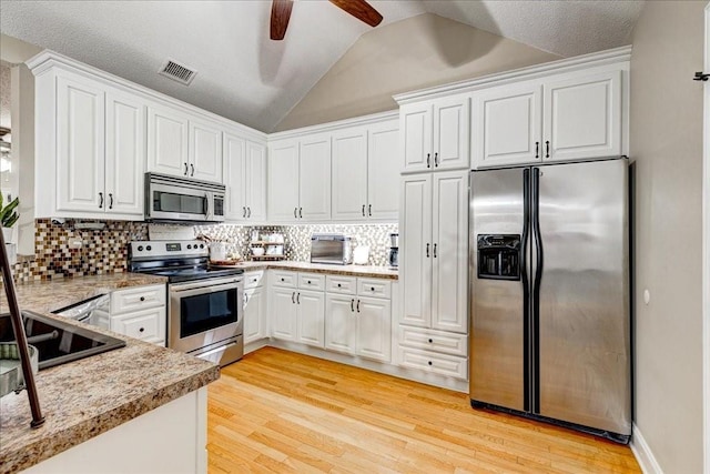 kitchen featuring lofted ceiling, light hardwood / wood-style flooring, appliances with stainless steel finishes, white cabinetry, and decorative backsplash