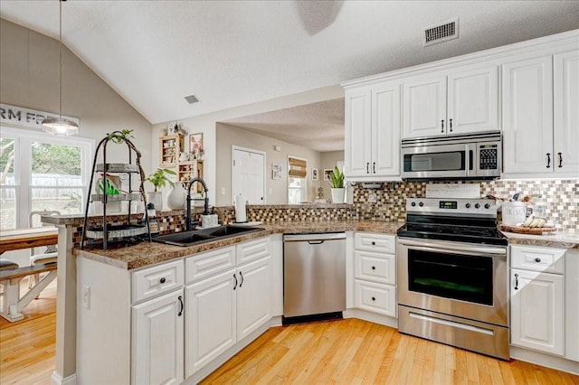 kitchen with appliances with stainless steel finishes, pendant lighting, sink, white cabinets, and kitchen peninsula