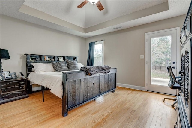 bedroom with ceiling fan, wood-type flooring, a raised ceiling, and access to outside