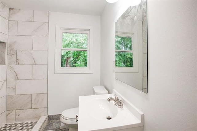 bathroom with a tile shower, toilet, and sink