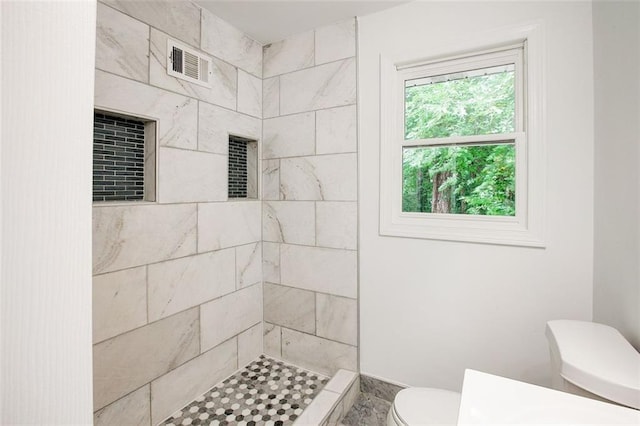 bathroom with a tile shower and toilet