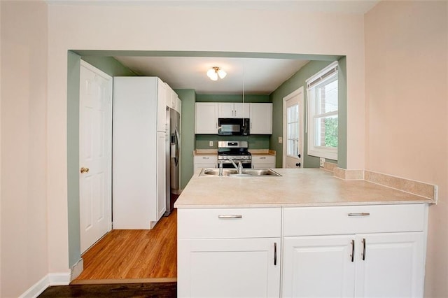 kitchen with appliances with stainless steel finishes, light hardwood / wood-style flooring, white cabinetry, and sink