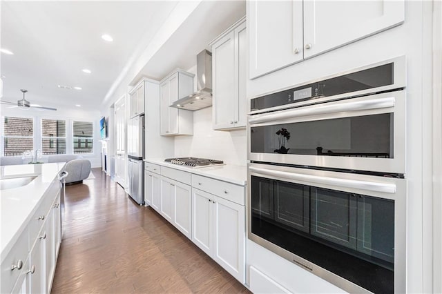 kitchen with wall chimney exhaust hood, dark hardwood / wood-style floors, ceiling fan, white cabinetry, and stainless steel appliances