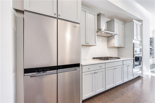 kitchen with white cabinetry, dark wood-type flooring, wall chimney range hood, backsplash, and appliances with stainless steel finishes