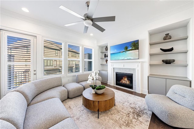 living room with ceiling fan, crown molding, hardwood / wood-style flooring, built in features, and a fireplace