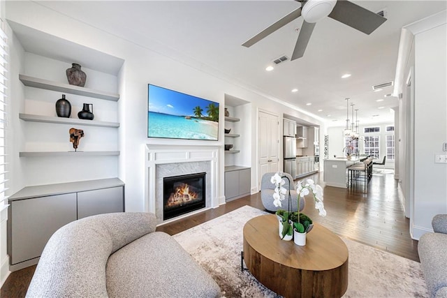 living room with built in shelves, a premium fireplace, hardwood / wood-style floors, and ceiling fan