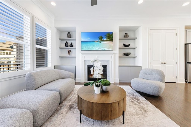 living room featuring crown molding, a premium fireplace, built in features, and wood-type flooring