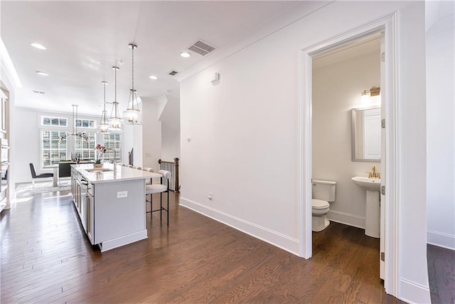 kitchen with dark wood-type flooring, decorative light fixtures, white cabinets, a center island, and a breakfast bar area