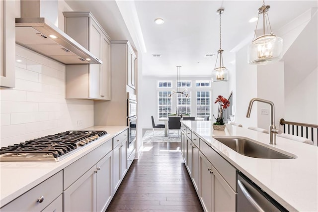 kitchen featuring tasteful backsplash, stainless steel appliances, sink, wall chimney range hood, and hanging light fixtures