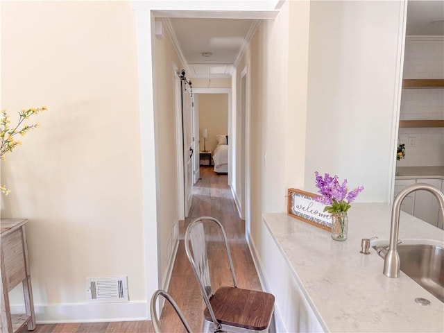 hall with ornamental molding, a barn door, sink, and hardwood / wood-style floors