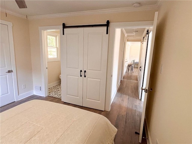 unfurnished bedroom featuring crown molding, connected bathroom, dark hardwood / wood-style floors, and a barn door