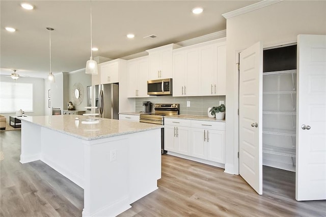 541 Fundao Ln, Lawrenceville, GA 30046 - kitchen with appliances with stainless steel finishes, crown molding, a kitchen island, white cabinets, and light wood-style flooring