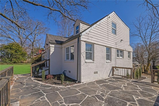 view of property exterior featuring crawl space, a patio, and brick siding