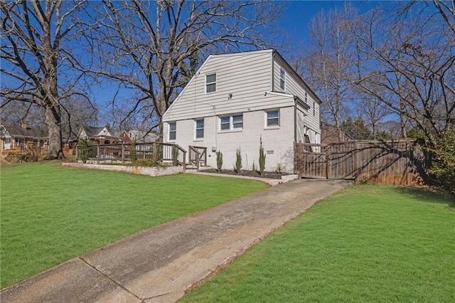 view of side of property with brick siding, a yard, a gate, fence, and a deck