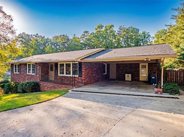 ranch-style home featuring brick siding, concrete driveway, fence, a carport, and a front yard