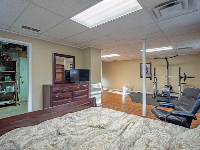 bedroom with a paneled ceiling, visible vents, baseboards, and wood finished floors